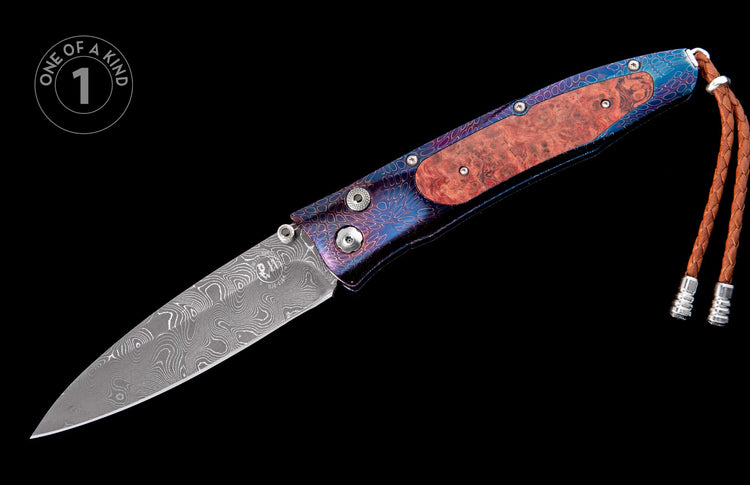 Folding knife with a Damascus blade, burl wood handle, blue and purple patterned metal, a brown braided leather lanyard, and a 'one of a kind' badge.