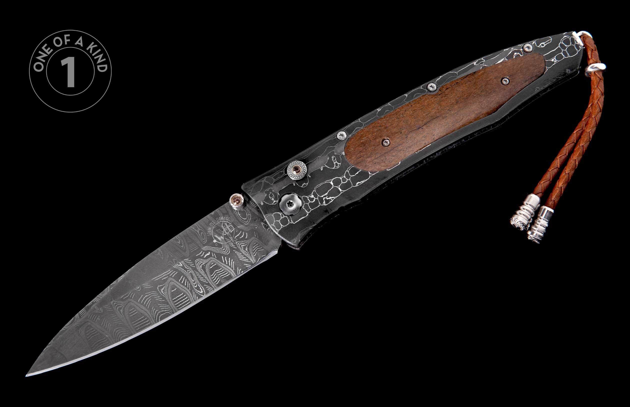 Folding knife with a patterned Damascus steel blade, dark etched frame, brown wood handle, and braided leather lanyard.