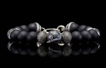 Black matte beaded bracelet with a central marbled bead and textured silver spacers, reflecting on a dark surface.