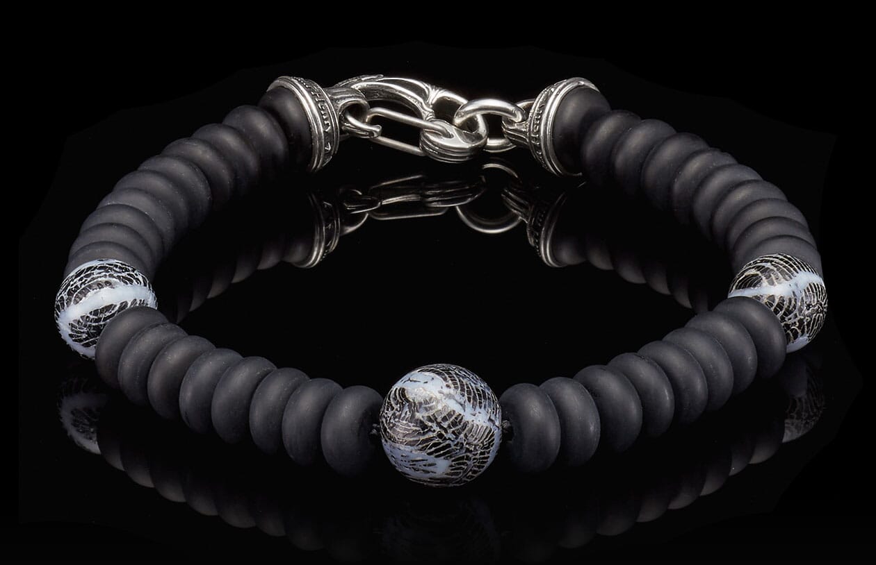 Matte black beaded bracelet with a silver hook clasp and three patterned white and black glass accent beads.