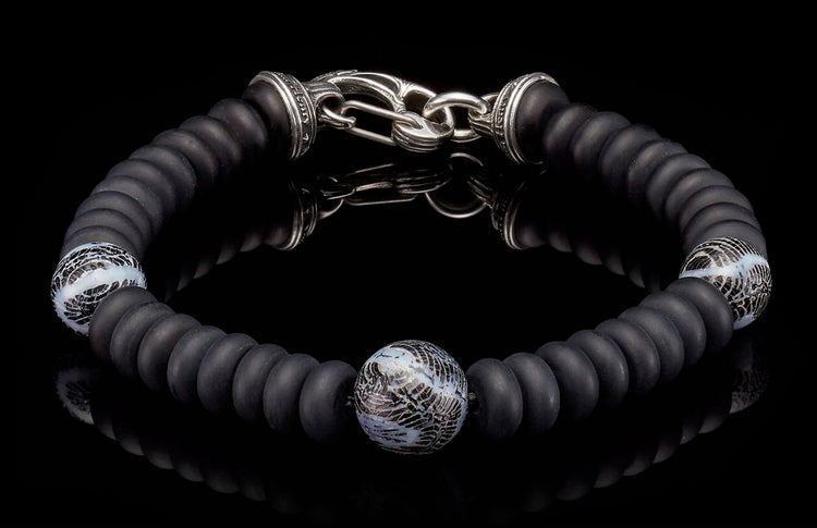 Matte black beaded bracelet with a silver hook clasp and three patterned white and black glass accent beads.