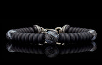 Black beaded bracelet with matte black and patterned grey beads, silver accents, reflecting on a dark surface.