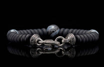 Matte black beaded bracelet with an ornate silver-tone clasp featuring engravings, a central patterned bead, and a strong reflection.