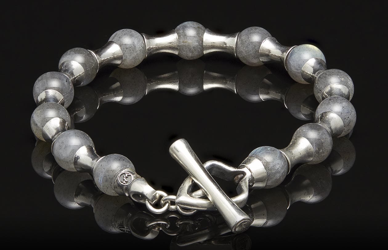Silver-tone beaded bracelet with grey stone beads, featuring alternating metal links and a toggle clasp, on a reflective surface.