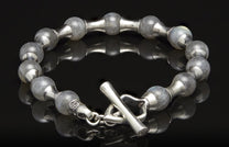 Silver-tone beaded bracelet with grey stone beads, featuring alternating metal links and a toggle clasp, on a reflective surface.