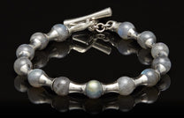 Silver bracelet with rounded labradorite beads and a toggle clasp, reflected on a black surface.