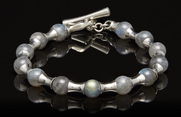 Silver bracelet with rounded labradorite beads and a toggle clasp, reflected on a black surface.