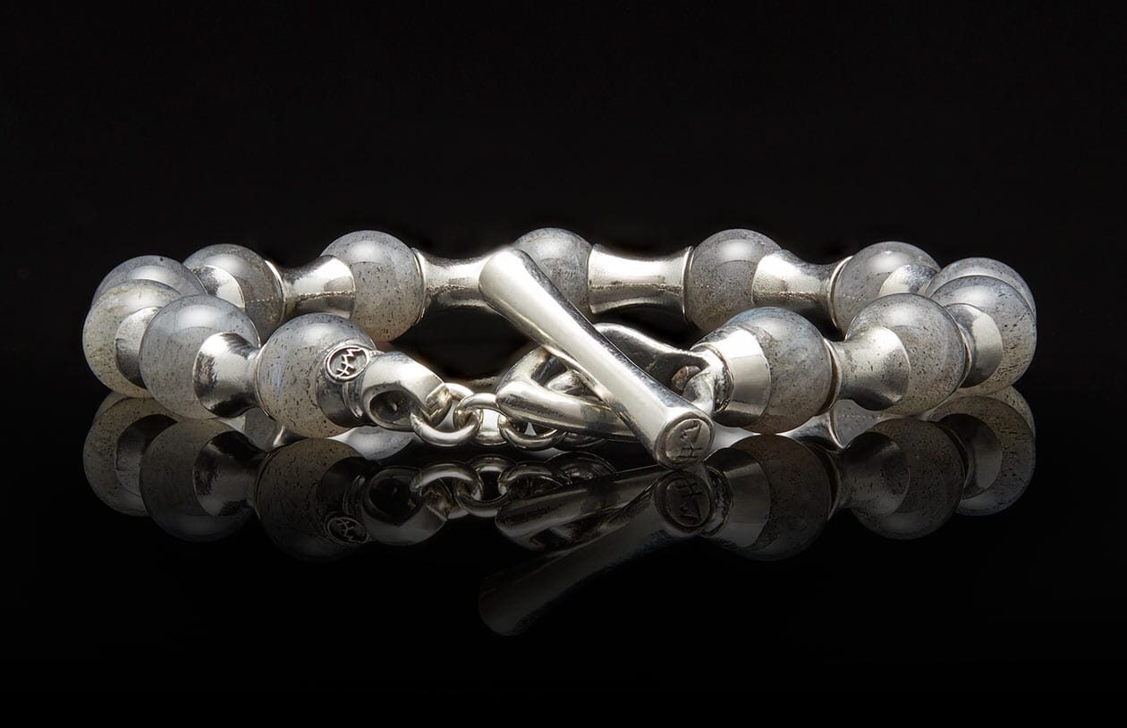 Silver bracelet with rounded, cloudy grey beads and an etched toggle clasp, reflected on a black surface.