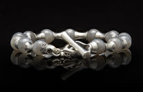 Silver bracelet with rounded, cloudy grey beads and an etched toggle clasp, reflected on a black surface.