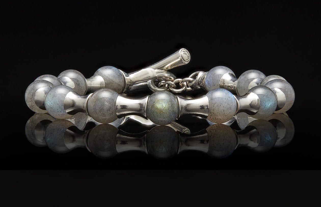 Silver and labradorite beaded bracelet with a toggle clasp on a reflective black surface.