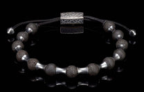 Lava stone bracelet with dark porous beads, silver-toned metal spacers, and a hammered rectangular clasp on a black reflective surface.