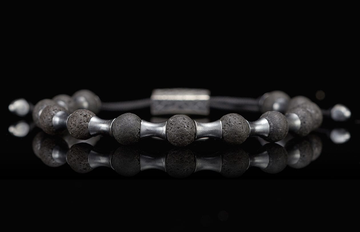 Dark lava stone and silver metal beaded bracelet featuring porous beads and reflective spacers on a black surface.
