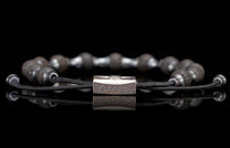 Dark gray lava stone beaded bracelet with a textured silver-toned metal clasp and adjustable black braided cords.