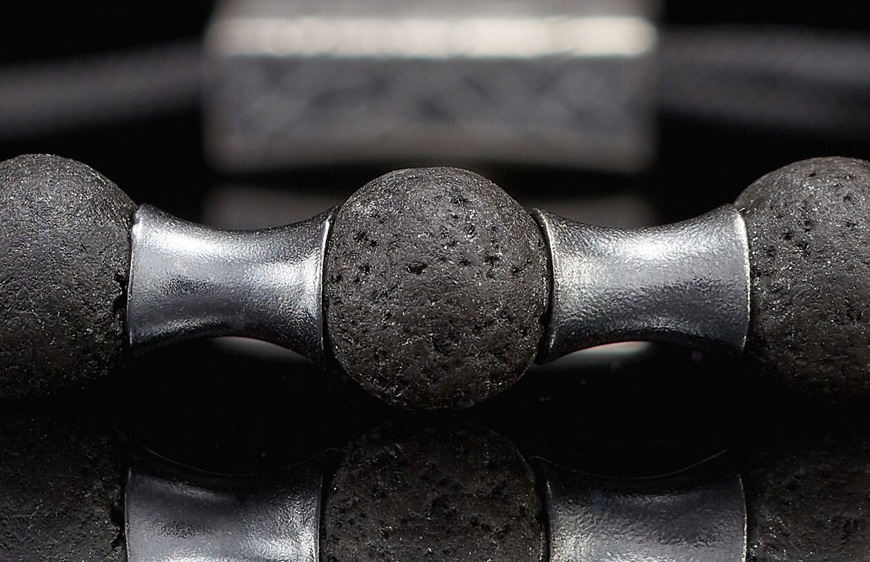 Close-up of a dark grey lava stone bracelet with textured beads and shiny silver metal separators.