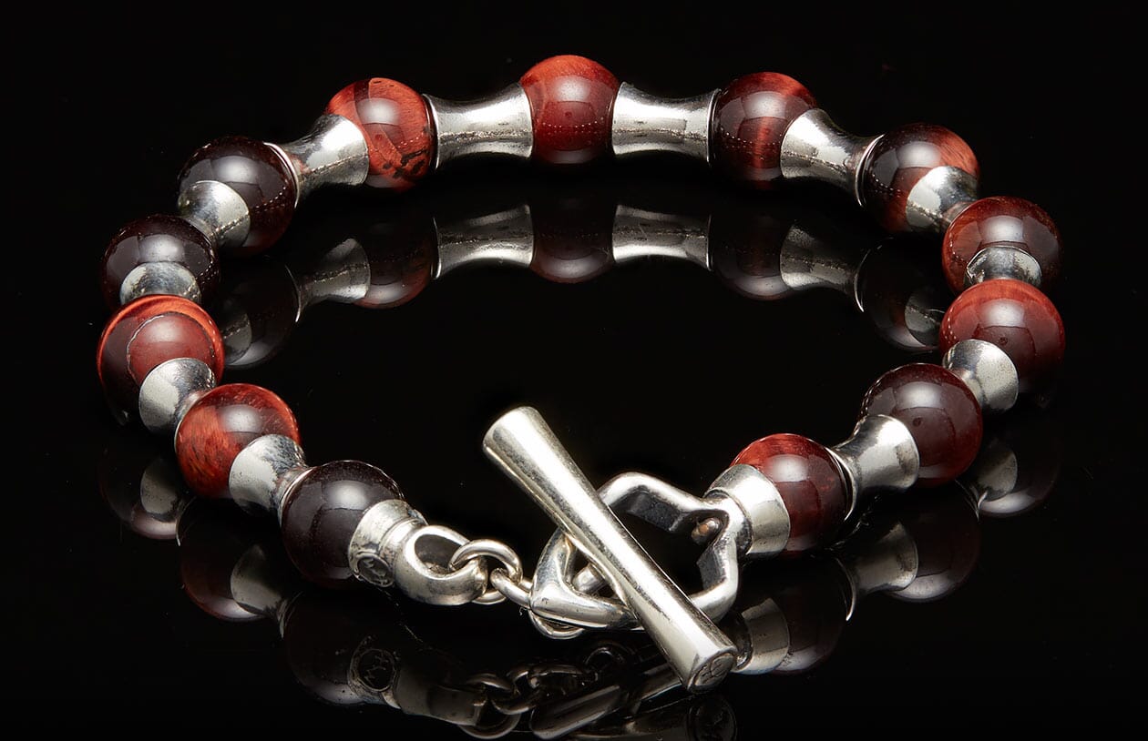 Red tiger's eye beaded bracelet with silver spacers and a toggle clasp on a black reflective surface.