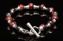 Red tiger's eye beaded bracelet with silver spacers and a toggle clasp on a black reflective surface.