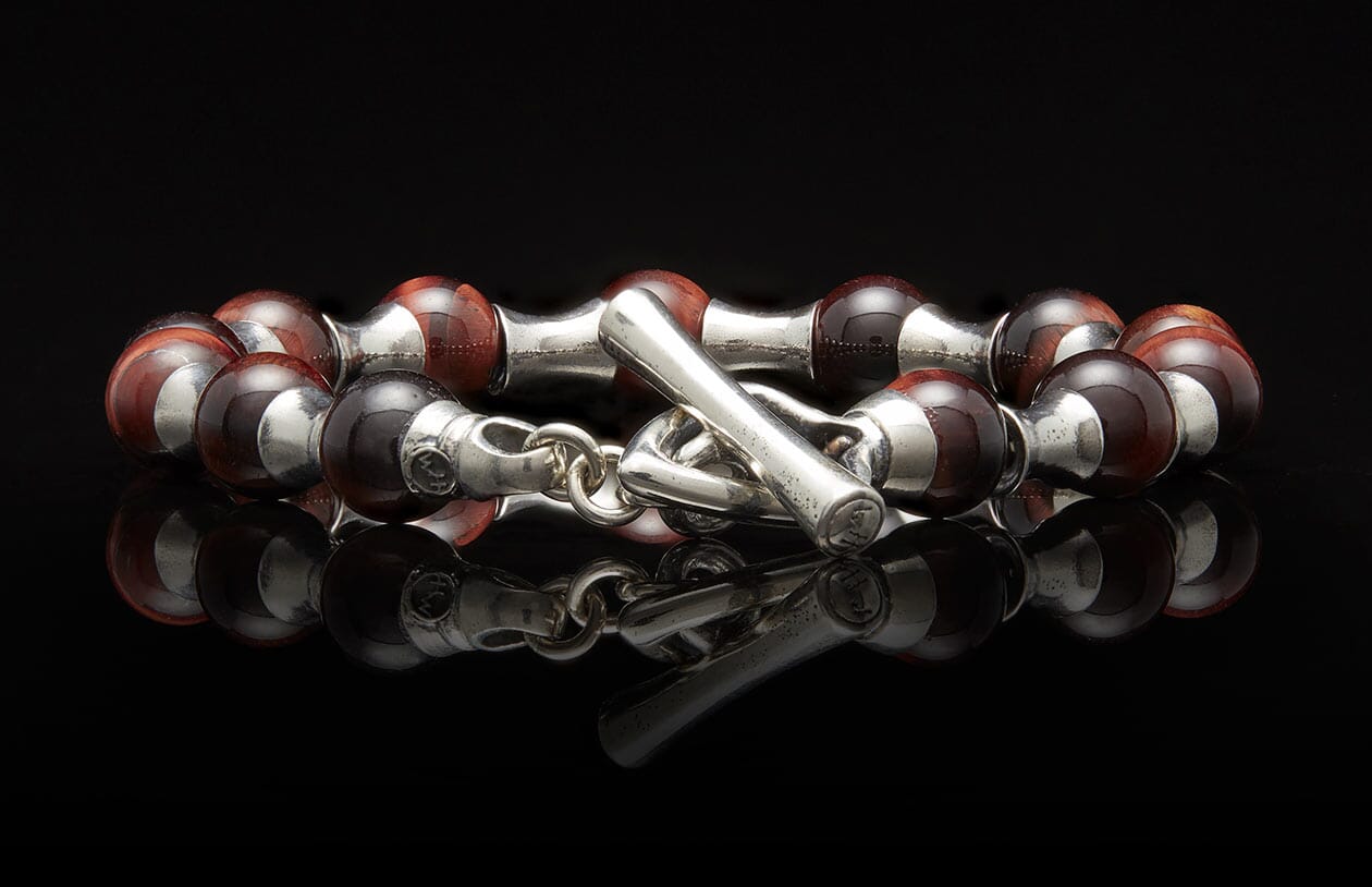 Beaded bracelet with reddish-brown and silver-colored beads, featuring a toggle clasp on a reflective surface.