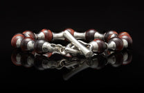 Beaded bracelet with reddish-brown and silver-colored beads, featuring a toggle clasp on a reflective surface.