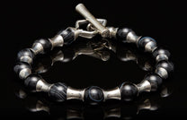 Silver and black beaded bracelet with a toggle clasp, featuring striped agate and smooth black beads separated by silver spacers on a reflective surface.