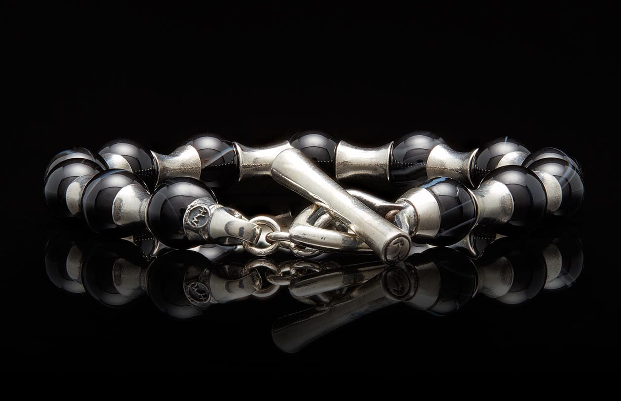 Black and silver beaded bracelet featuring polished black and white striped agate beads and a silver toggle clasp on a reflective surface.
