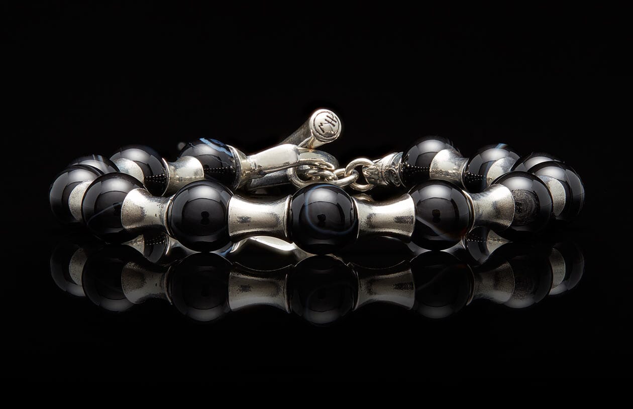 Black agate bead and silver spacer bracelet with a distinctive toggle clasp, reflecting on a dark surface.