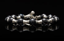 Black agate bead and silver spacer bracelet with a distinctive toggle clasp, reflecting on a dark surface.