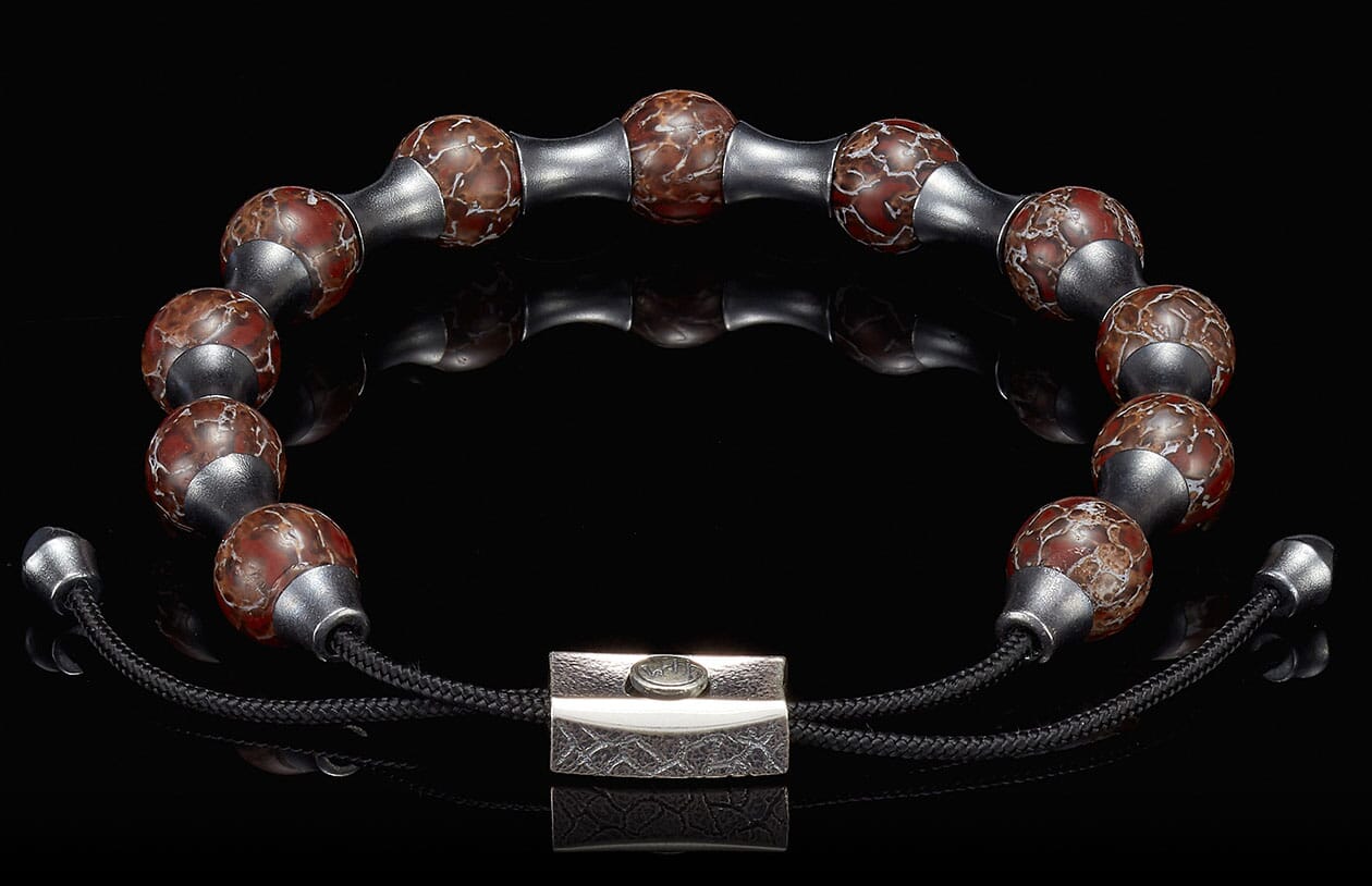 Bracelet with reddish-brown crackled beads, matte silver spacers, and a textured rectangular clasp on a reflective surface.