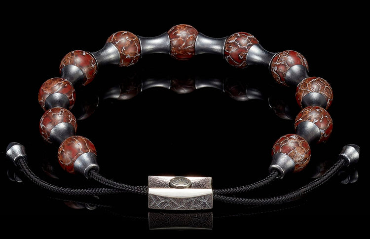 Bracelet with reddish-brown crackled beads, matte silver spacers, and a textured rectangular clasp on a reflective surface.