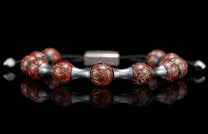 Beaded bracelet with red-brown marbled beads, silver tube spacers, and a central rectangular clasp, reflected on a dark surface.