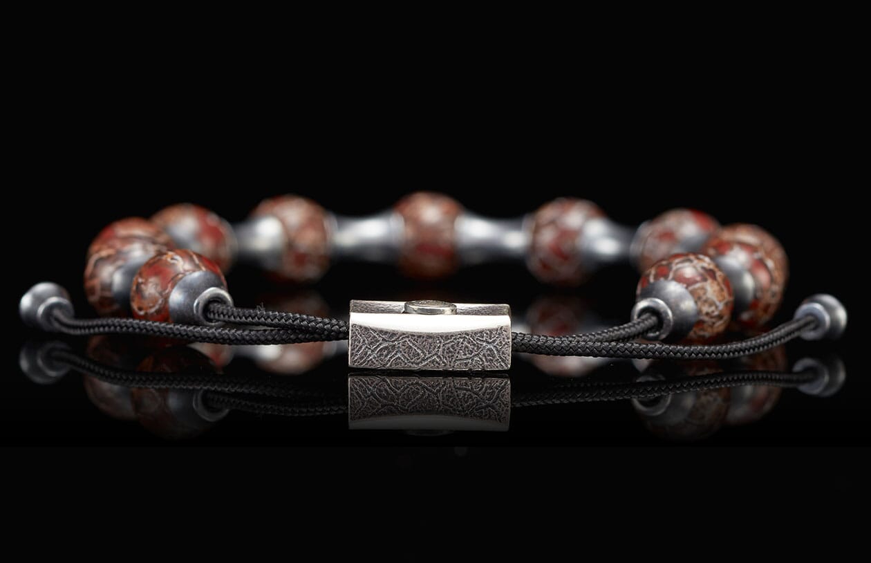 Beaded bracelet with red and gray patterned stones, a silver-toned textured centerpiece, and black cords.
