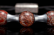 Reddish-brown stone beaded jewelry with white fossil-like patterns and silver metallic spacers, reflected on a dark surface.