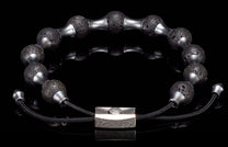 Black lava stone and silver-toned metal bracelet with textured beads and a rectangular patterned clasp on a reflective black surface.