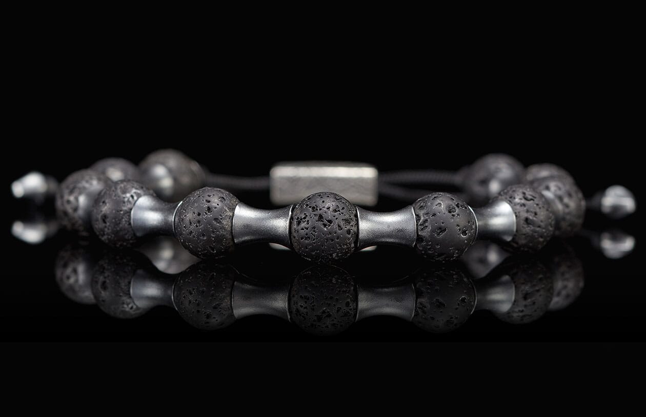 Black lava stone bracelet with silver metal barbell-shaped spacers, featuring porous texture and a reflective surface.