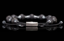 Black lava stone bracelet with an intricately engraved silver clasp, reflected on a glossy surface.