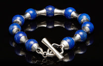 Lapis lazuli and silver beaded bracelet with a toggle clasp, reflecting on a dark surface.