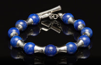 Blue lapis lazuli and silver bracelet with a toggle clasp, lying on a reflective black surface.