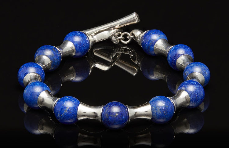 Blue lapis lazuli and silver bracelet with a toggle clasp, lying on a reflective black surface.