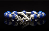 Blue lapis lazuli and silver beaded bracelet with a T-bar clasp, reflecting on a dark surface.