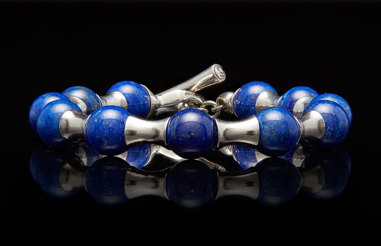 Lapis lazuli and silver beaded bracelet with a toggle clasp on a reflective black surface.