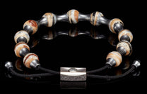 Beaded bracelet with variegated brown and cream mammoth ivory beads, dark metal spacers, black cord, and a textured silver clasp.