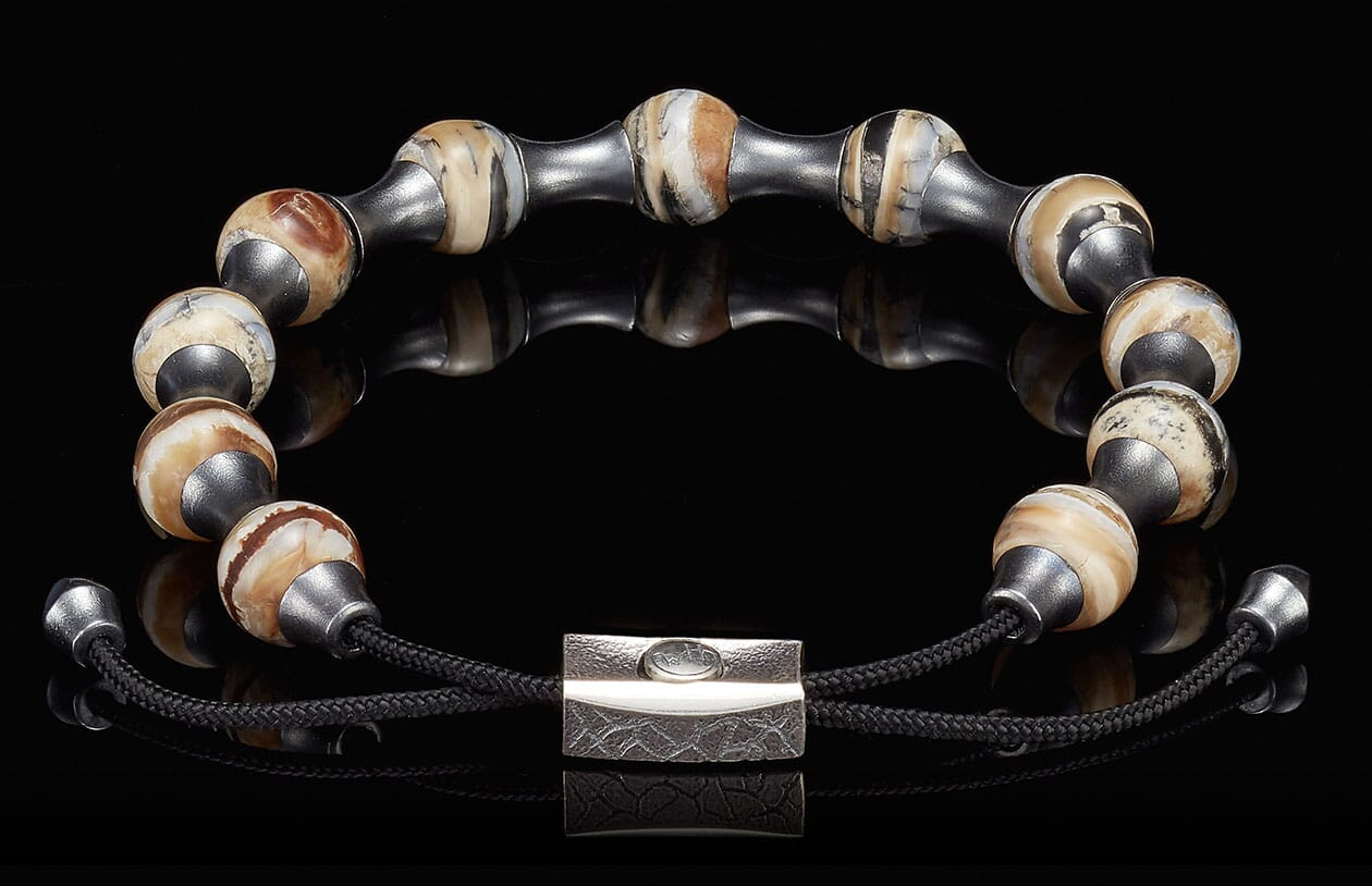 Beaded bracelet with variegated brown and cream mammoth ivory beads, dark metal spacers, black cord, and a textured silver clasp.