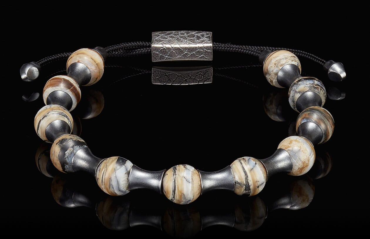 Adjustable bracelet with spherical, naturally banded beads in cream, brown, and black, dark metal spacers, and a hammered clasp.
