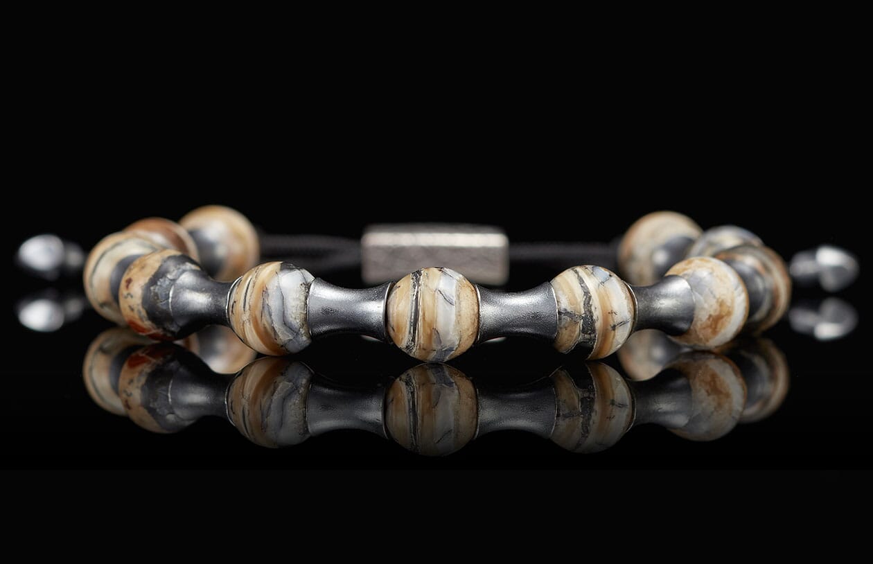 Mammoth Zenith bracelet with striped beige, black, and grey stone beads and dark metal spacers on a reflective surface.