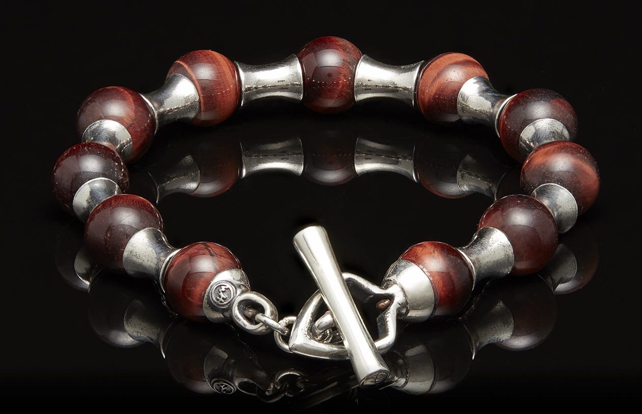 Red tiger eye and silver beaded bracelet with a toggle clasp, reflecting on a dark surface.