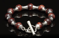 Red tiger eye and silver beaded bracelet with a toggle clasp, reflecting on a dark surface.