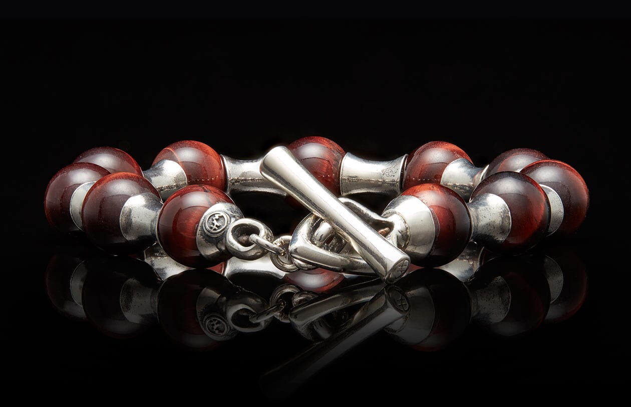 Reddish-brown beaded bracelet with silver end caps and a prominent toggle clasp on a reflective surface.