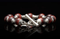 Reddish-brown beaded bracelet with silver end caps and a prominent toggle clasp on a reflective surface.