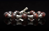 Polished reddish-brown beaded bracelet with chatoyant streaks and silver accents, featuring a toggle clasp, reflected on a black surface.