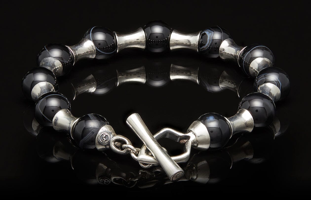 Black agate bead bracelet with silver spacers and a toggle clasp, lying on a reflective surface.
