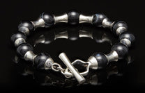 Black agate bead bracelet with silver spacers and a toggle clasp, lying on a reflective surface.